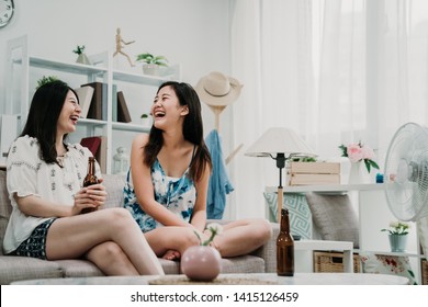 Cheerful Young Girl Friends Drinking Ice Cold Beer Talking Sitting Indoors At Home. Laughing Women On Couch Sofa By Fan During Hot Weather In Summer In Cozy Apartment Having Fun Gossip Chatting