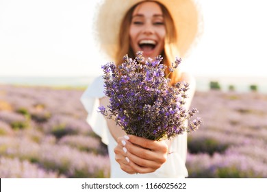 Cheerful young girl in straw hat holding lavender bouquet at the field
