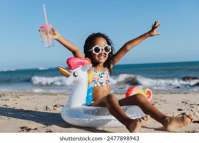 Cheerful young girl with sunglasses and unicorn float relaxing at the beach, holding a drink, and having fun during a summer vacation. - Powered by Shutterstock