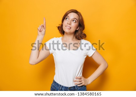 Cheerful young girl wearing t-shirt standing isolated over yellow background, pointing at copy space