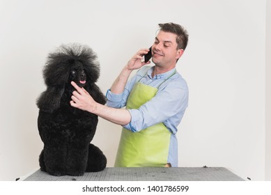 Cheerful Young Groomer Talking On A Phone With Poodle's Owner