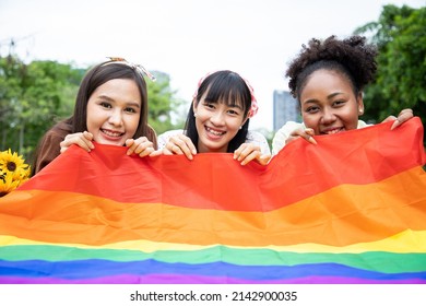 Cheerful Young Group Of Women With Rainbow Flag At Gay Pride While Leisure In The Park. Concept Of Homophobia And Diversity Lesbians. Supporters Of The LGBT Community