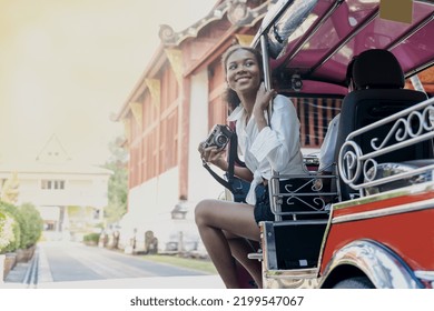 Cheerful young half african independent tourist girl sitting in TUKTUK taxi beside tuktuk driver holding camera enjoy travelling at Wat Pra Singh Chiangmai,Thailand,travel and summer vacation concept