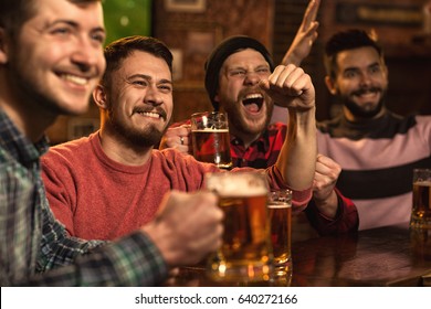 Cheerful young handsome male friends having fun at the beer pub celebrating victory of their favorite team watching game on TV happiness people leisure entertainment bar restaurant friendship