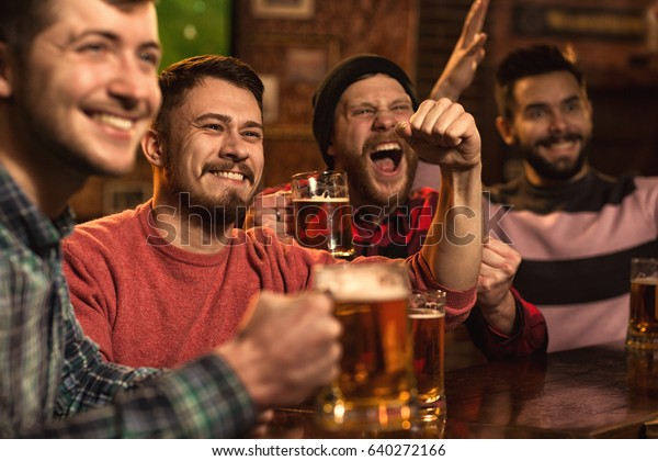 Cheerful\
young handsome male friends having fun at the beer pub celebrating\
victory of their favorite team watching game on TV happiness people\
leisure entertainment bar restaurant\
friendship