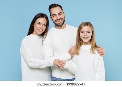 Cheerful young happy parents mom dad with child kid daughter teen girl in basic white sweaters hugging holding hands isolated on blue color background studio portrait. Family day parenthood concept