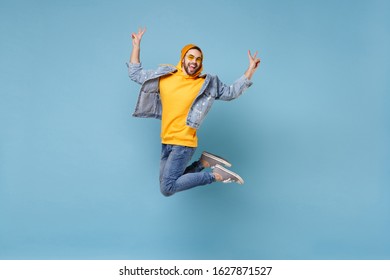 Cheerful young hipster guy in fashion jeans denim clothes posing isolated on pastel blue background in studio. People lifestyle concept. Mock up copy space. Jumping, screaming, showing victory sign - Shutterstock ID 1627871527