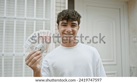 Cheerful young hispanic teenager confidently flashing a wad of iceland krona banknotes with a dazzling smile on a bustling city street, revealing an empowering expression of financial joy