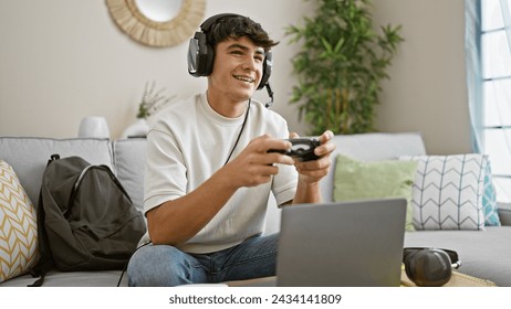 Cheerful, young hispanic teenager student, gamepad in hand, engrossed in online gaming, lounging on living room sofa, making his apartment a lively gaming house. - Powered by Shutterstock