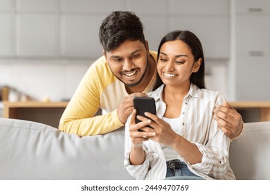 A cheerful young Indian couple intimately huddled looking at a smartphone, possibly sharing a moment of digital connection - Powered by Shutterstock