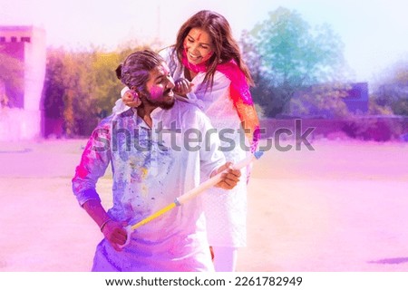 Cheerful young Indian couple playing with colorful powder color or gulal celebrating holi festival at park outdoor.