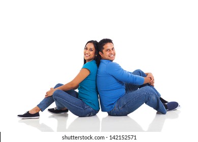 cheerful young indian couple sitting back to back on floor