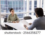 Cheerful young Indian job candidate speaking to recruit manager, employer at interview, discussing paper resume. Couple of happy business colleagues, partners talking at meeting table