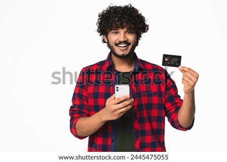 Cheerful young Indian man paying with credit card in mobile application online isolated over white background. Hindi bank customer doing online shopping in cellphone