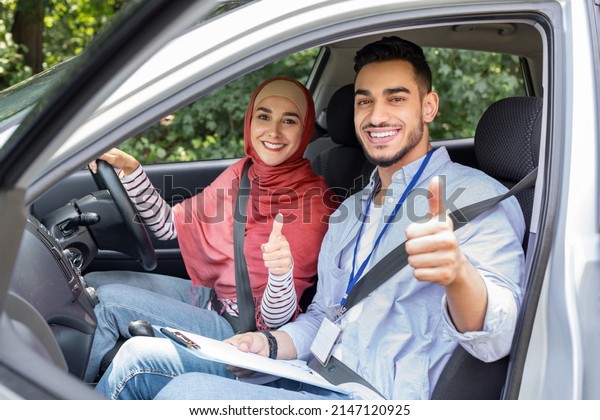 Cheerful young islamic and woman in hijab at\
steering wheel in car show thumbs up in cabin auto, outdoor.\
Student take driving test good, driving class and lesson in traffic\
at city, great result