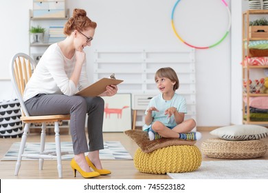 Cheerful Young Kid Talking With Helpful Child Counselor During Psychotherapy Session In Mental Health Center For Children