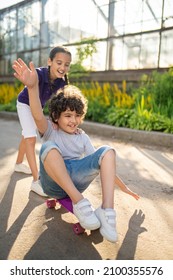 Cheerful young lady playing with her friend during his skateboarding