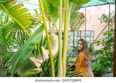 Cheerful young lady in a yellow dress amidst vibrant tropical plants in a greenhouse - Powered by Shutterstock