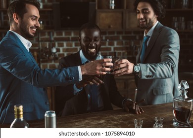 Cheerful Young Male Friends In Suits Clinking Glasses Of Whiskey