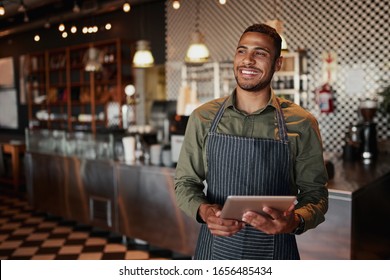 Cheerful young male owner holding digital tablet while standing in cafe - Powered by Shutterstock