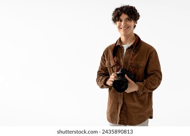 Cheerful young male photographer with curly hair, wearing corduroy jacket, holds professional DSLR camera, ready for photo shoot, white background with free space - Powered by Shutterstock