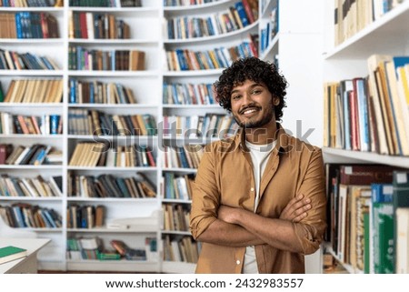 A cheerful young man with curly hair stands confidently with his arms crossed in a well-stocked library. He projects a vibe of intelligence and positivity amidst a collection of books.
