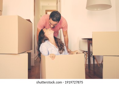 Cheerful young man dragging box with his girlfriend inside and kissing her. Joyful family couple having fun while moving into new flat. New home concept