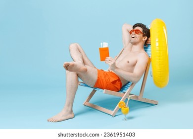 Cheerful young man guy in orange shorts glasses sit on deck chair isolated on pastel blue background studio. People summer vacation rest lifestyle concept. Mock up copy space. Hold passport tickets - Shutterstock ID 2361951403
