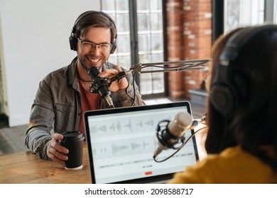 Cheerful young man in headphones looking at camera, smiling, speaking in microphone in podcasting studio while have an interview. Radio host interviewing famous blogger for online show on her channel - Powered by Shutterstock