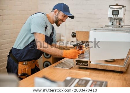 Cheerful young man repairing coffee machine in cafe