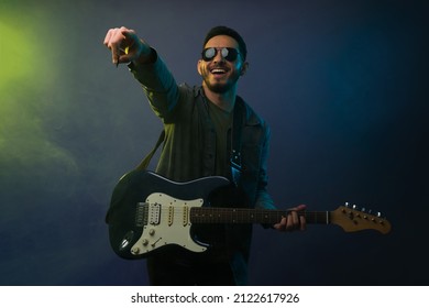 Cheerful young man and rock singer pointing to the crowd while singing and playing the electric guitar  - Powered by Shutterstock