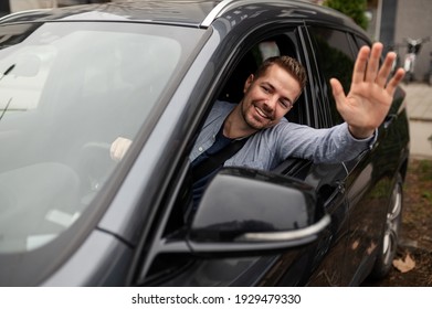 Cheerful young man saying hello, waving his hand while he drives  his new car slowly 