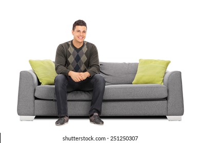 Cheerful young man sitting on a modern sofa isolated on white background