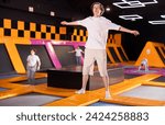 Cheerful young man in sportswear bouncing and jumping on trampolines indoors in leisure sports center indoors