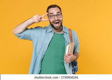 Cheerful young man student in casual clothes glasses with backpack hold books isolated on yellow background studio portrait. Education in high school university college concept. Showing victory sign