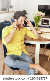 Cheerful Young Man Talking With Someone, Using Smartphone While Relaxing At Home. Handsome Happy Guy. Real People Lifestyle.