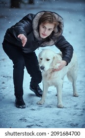 Cheerful Young Man In Trendy Black Leather Jacket Walks His Dog In A Winter Park On A Snowy Day. Men's Winter Fashion. Happy Owner And His Pet Dog. Full Length Shot.