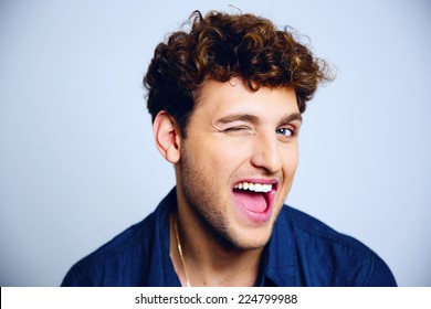 Cheerful young man winking over blue background