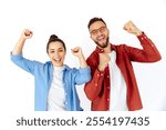 Cheerful young man and woman, celebrating success with raised arms, smiling brightly, expressing excitement and positivity, dressed casually, stand on isolated white background, laughing