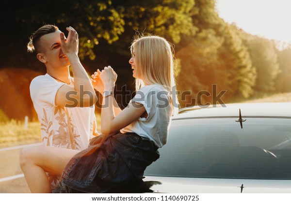 Cheerful young man and woman laughing at car parked at\
roadside in nature 