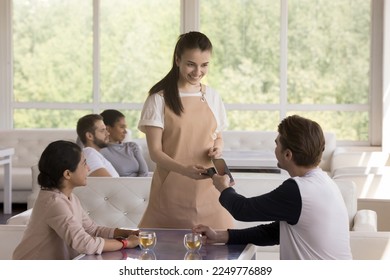 Cheerful young man and woman paying bill in cafe, connecting cellphone with payment terminal offered by waitress for electronic transaction. Happy diverse couple drinking tea in coffee shop. - Powered by Shutterstock