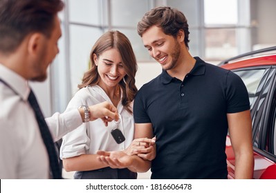 Cheerful young man and woman receiving keys of new automobile from professional dealer in car salon - Shutterstock ID 1816606478