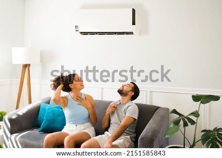 Cheerful young man and woman relaxing on the sofa with the best air conditioner and enjoying the cold air flow 