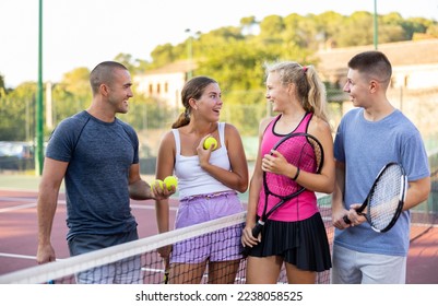 Cheerful young men and women tennis players standing on outdoor court together and talking. - Powered by Shutterstock