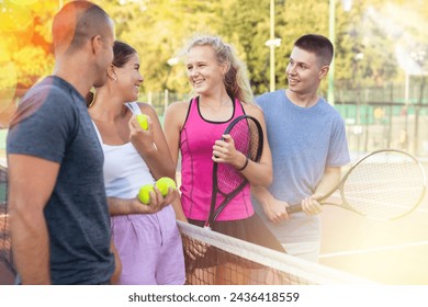 Cheerful young men and women tennis players standing on outdoor court together and talking. - Powered by Shutterstock