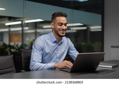 Cheerful Young Middle Eastern Manager Sitting At Worktable At Modern Office, Typing On Notebook Keyboard, Sending Emails To His Business Partners, Working On Marketing Research, Copy Space