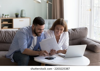 Cheerful young millennial husband and wife doing domestic paperwork, accounting job, reviewing paper bills, receipts at laptop computer, using calculator, paying mortgage, rent fees on internet