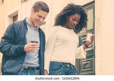 Cheerful young mix raced couple walking outdoors and minding their steps. Happy Caucasian man and black woman with takeaway coffee holding hands and looking down. Watching steps concept - Powered by Shutterstock