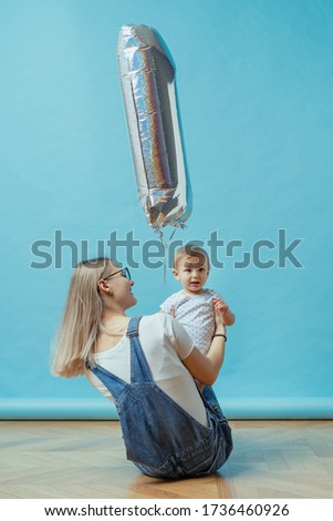 Cheerful young mom celebrate first birthday with her one year kid on blue background