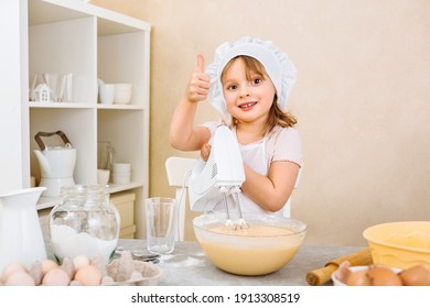 A cheerful young mother's assistant kneads the dough for a pie with a mixer, performs a step-by-step recipe on a tablet on the Internet, for a happy family holiday at home.